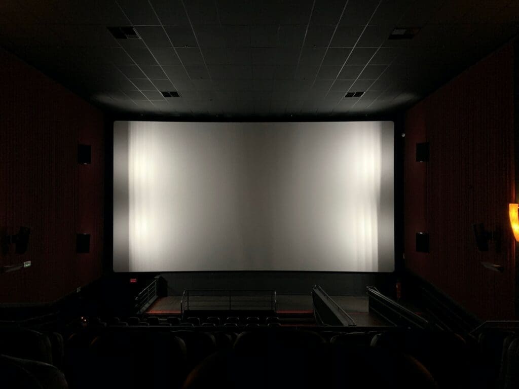Teatro en penumbras con asientos vacíos y la escala de grises LED reflejada en una enorme pantalla